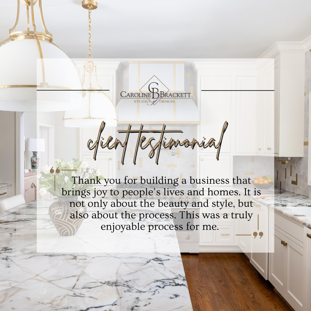 Bright, white kitchen with marble countertops, white cabinets, four hanging pendant lights, and a decorative vase with flowers on the island.